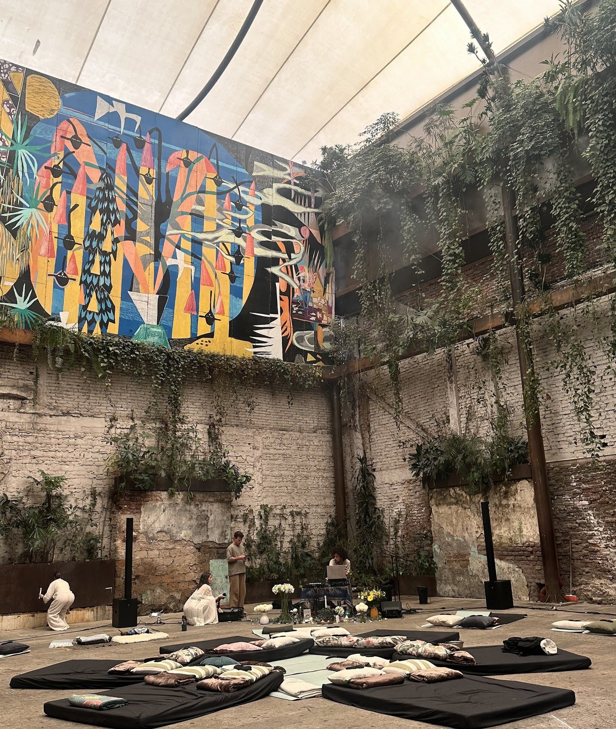 Last year's gathering: a courtyard in Mexico City with a painted mural, ivy-covered brick, and mats laid out for a session